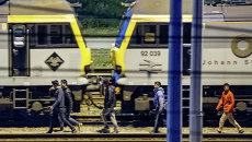 Мигранты идут вдоль железнодорожных путей в терминале Евротуннеля Мигранты идут вдоль железнодорожных путей в терминале Евротуннеля