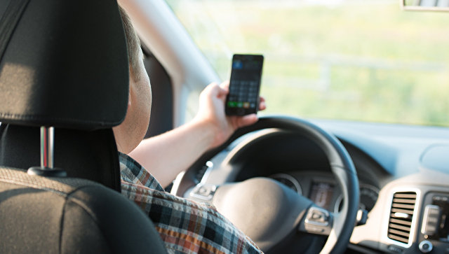 Молодой человек пользуется мобильным телефоном за рулем автомобиля. Архивное