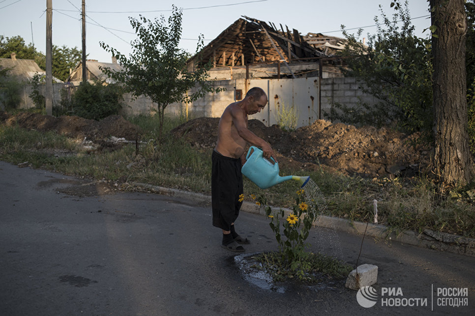 Мужчина поливает цветы на одной из улиц поселка Веселое Донецкой области